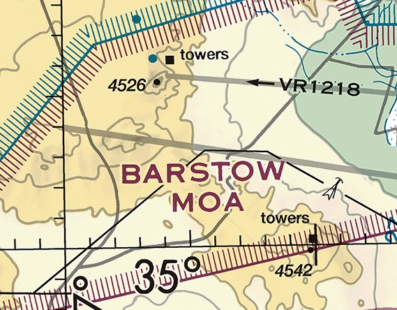 Sectional chart excerpt of the Mojave Desert. A thin gray line runs left to right across the upper part of the frame, carrying a solid black leftward arrowhead followed by the designator VR1218 in solid black type. Below it the words BARSTOW MOA are printed in large magenta capitals.