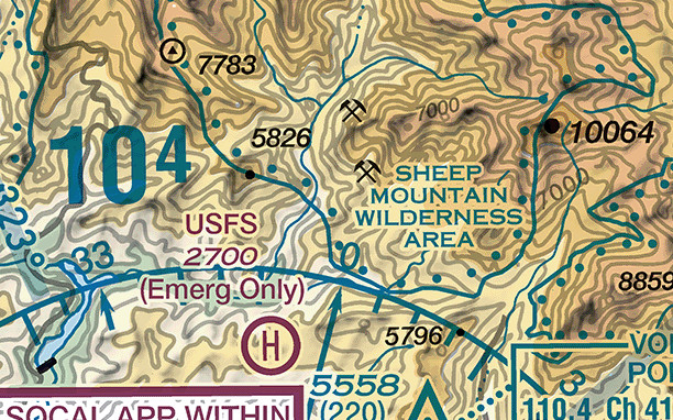 A sectional chart excerpt of a mountain range, printed in tan and brown bands with pale green in the valleys. Fine brown contour lines wind across the whole frame, closely packed on the steep slopes and labelled 7000 in two places. A large blue numeral 104 stands at the left, its final digit printed smaller and raised. Black numerals beside heavy black dots read 10064 at the right and 5826 and 5796 in the middle. At the top left a black circle containing a solid triangle marks a lookout tower, with its base elevation 7783 beside it. Near the bottom edge an obstruction symbol prints 5558 with 220 in parentheses below it. Green dotted boundaries enclose an area labelled Sheep Mountain Wilderness Area, a magenta airport named USFS prints its elevation 2700 with the note Emerg Only, and a magenta circled H marks a heliport.