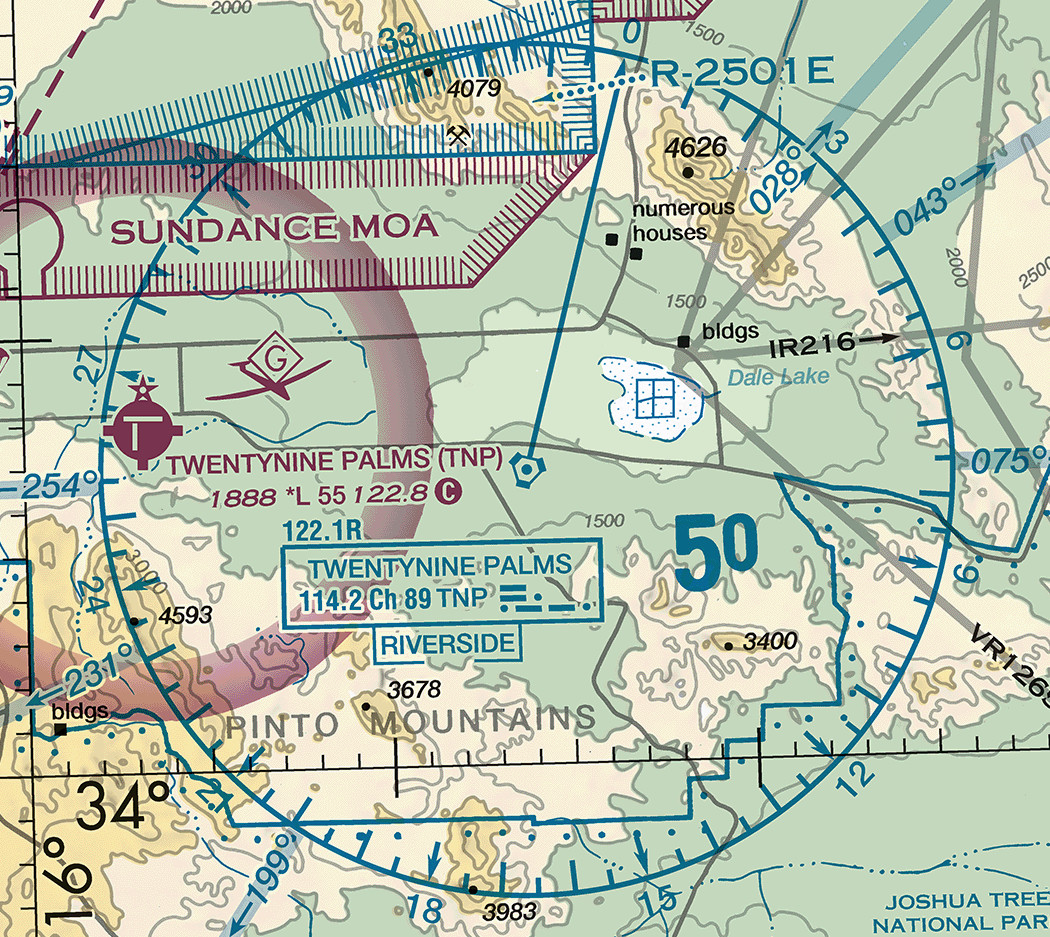 A sectional chart excerpt of open desert dominated by a large blue circle about two-thirds the width of the frame. The circle's rim is graduated with fine tick marks and labelled at intervals with the numerals 0 at the top, then 3, 6, 9, 12, 15, 18, 21, 24, 27, and 33 running clockwise around it. At the center sits a small blue hexagonal navigation aid symbol. Below and left of the center, a boxed legend reads TWENTYNINE PALMS on its first line and 114.2, Ch 89, TNP followed by dot and dash groups on its second, with 122.1R printed above the box and a second smaller box below reading RIVERSIDE. An airport named TWENTYNINE PALMS with TNP in parentheses prints in magenta at the left with the numbers 1888, an asterisk L, 55, 122.8 and a circled C. A magenta hatched boundary labelled SUNDANCE MOA crosses the top left, a blue hatched boundary labelled R-2501E crosses the top right, and gray lines labelled IR216 and VR1263 cross the right side.