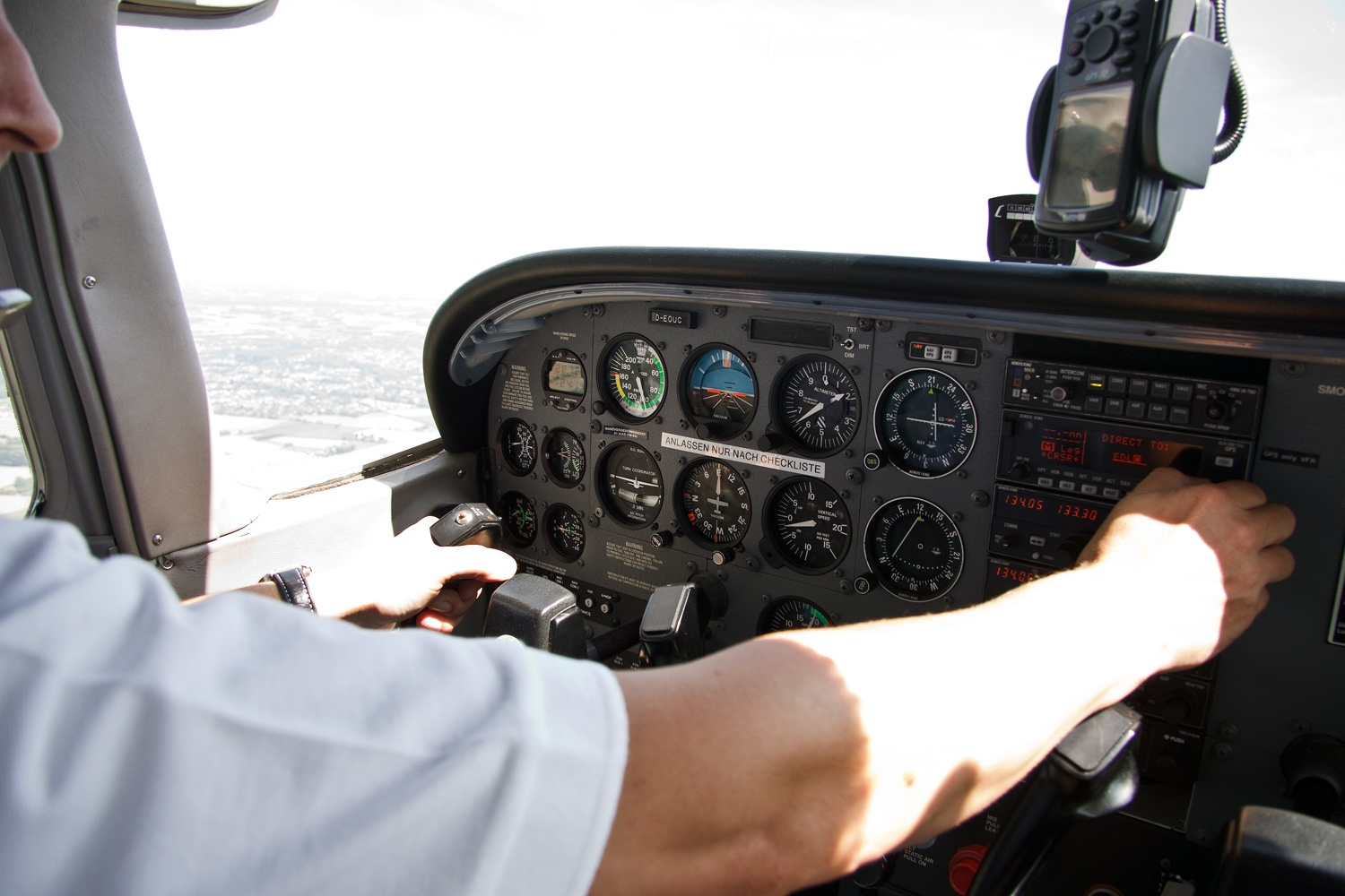 A pilot's hand on the yoke of a Cessna 172 in flight, with the instrument panel and horizon visible